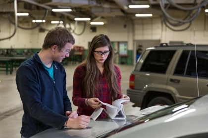 Students inspecting paperwork on trunk lid of car