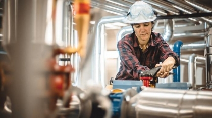 Woman in hardhat working on stainless steel pipes