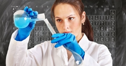 Woman in lab coat and rubber gloves pouring blue liquid from flask into test tube