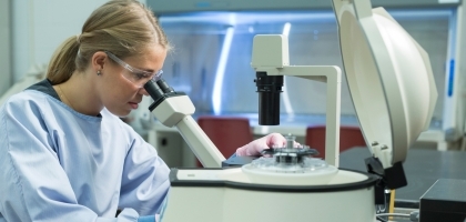Woman in surgical gown inspecting sample through microscope
