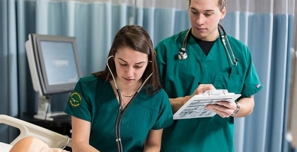 Two nurses over a patient in a bed, with stethoscopes and a clipboard